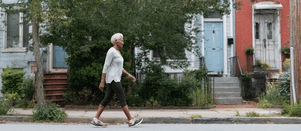 Active senior woman walking briskly through a neighborhood street, demonstrating low-impact cardio exercise for aging joints