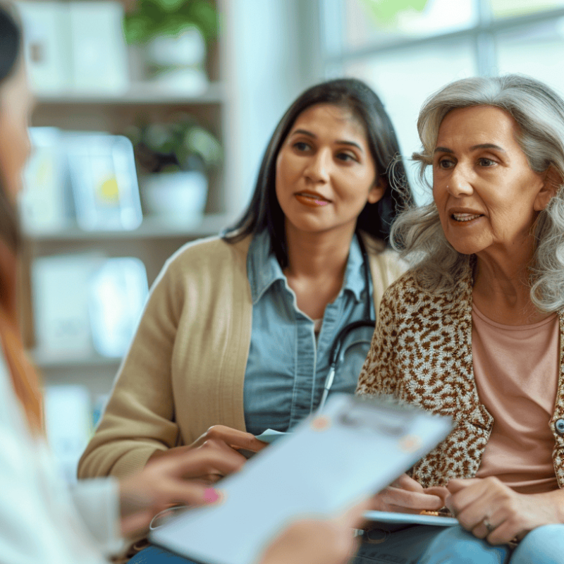 Adult daughter and elderly mother meeting with a patient advocate in a doctor's office